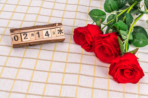 The small fresh style table top is covered with plaid cloth and a desk calendar and roses