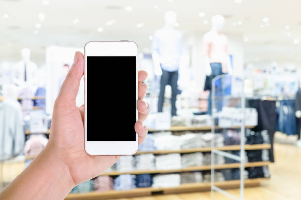 istock Man hand holding and using blank screen mobile smart phone with blurred background fashion shop in shopping mall 1006367650