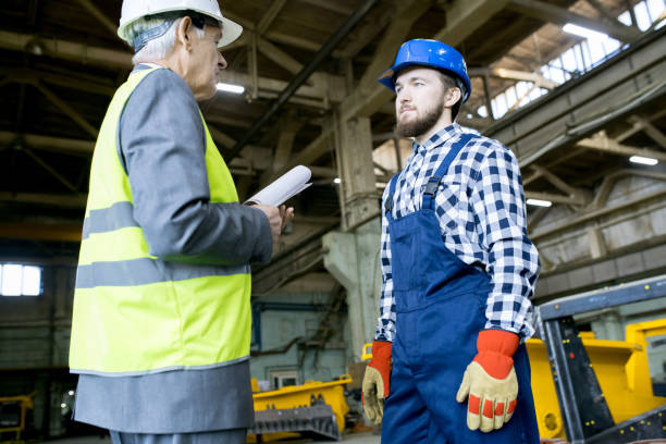 istock Serious confident senior executive and young bearded chief engineer talking about production and standing at factory workshop 1006371096