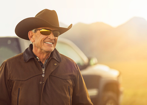 High quality stock photo of a modern cowboy wearing a black hat, sunglasses in early morning light.