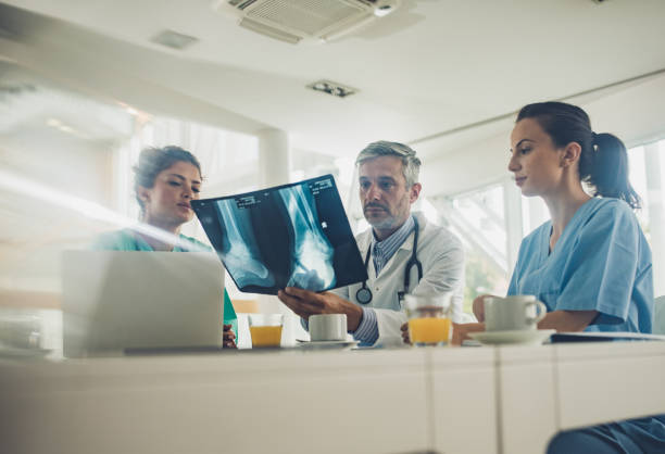 istock Male doctor and two nurses examining X-ray image at doctor's office. 1006430172