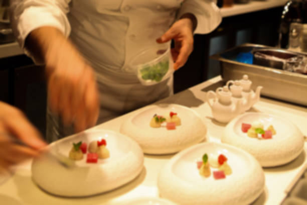 istock Blurred. Professional Starred Chef in action: plating an exquisite dessert in a white stylish bowl. Defocus. 1006452208