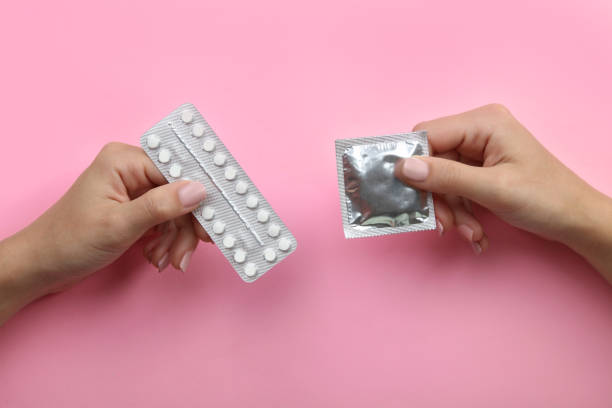 Contraceptive means: a condom and birth control pills Contraceptive means: a condom and birth control pills in a hand on a pink background. contraceptive photos stock pictures, royalty-free photos & images