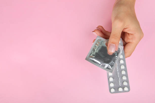 Contraceptive means: a condom and birth control pills Contraceptive means: a condom and birth control pills in a hand on a pink background. contraceptive photos stock pictures, royalty-free photos & images