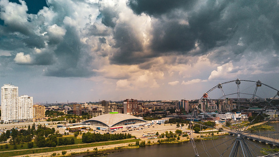 Aerial drone panoramic view of Chelyabinsk city, embankment of Miass river and Ferris wheel, smoking pipes on the background in cloudy day, Russia