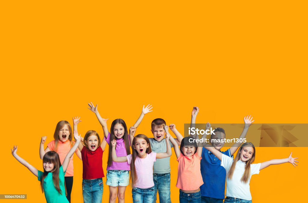 Happy success teensl celebrating being a winner. Dynamic energetic image of happy children We won. Winning success happy teen girls and boys celebrating being a winner. Dynamic image of caucasian Children on orange studio background. Victory, delight concept. Human facial emotions concept. Trendy colors Child Stock Photo