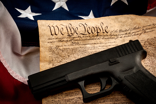 The second amendment and gun control in america concept with a handgun and the american constitution on the USA flag with close up on the 