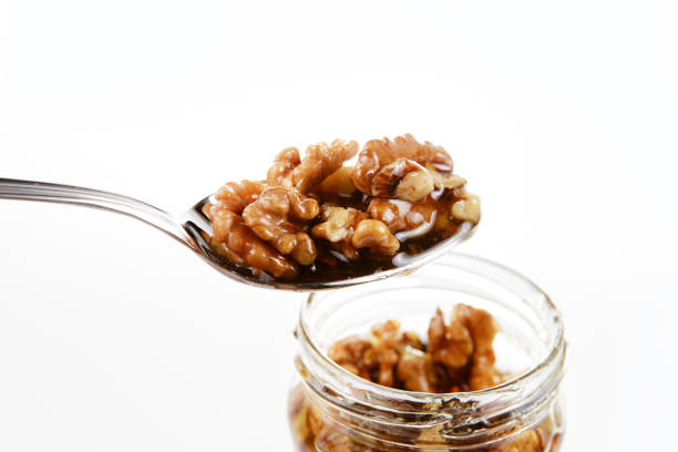 glas mit süßem honig und walnüssen mit silbernen löffel auf einem weißen hintergrund. gesundheit und schönheit-konzept. - syrup jar sticky isolated objects stock-fotos und bilder