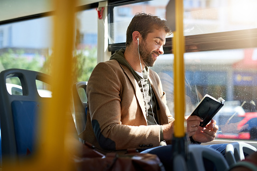 Cropped shot of a handsome young man reading a book during his morning bus commute