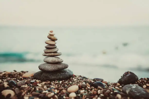 Photo of Stones balance and wellness retro spa concept. Close-up pyramid from stones stack over sea. cinematic toning.