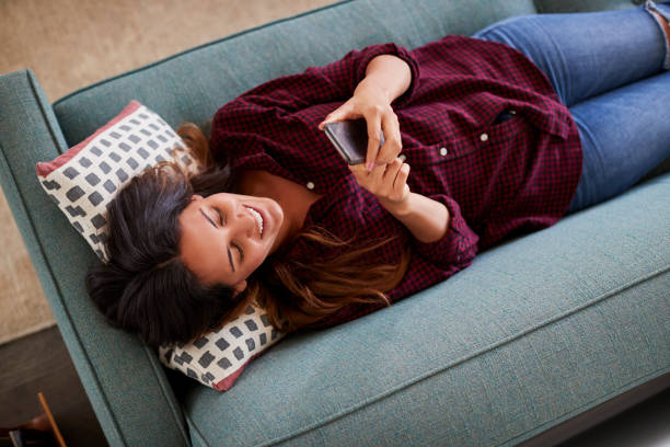 istock Overhead View Of Woman Lying On Sofa At Home Using Mobile Phone 1006535408