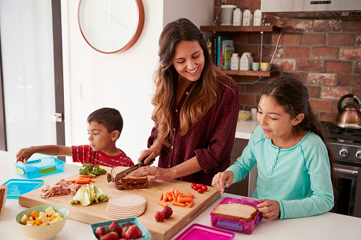 Niños ayudando a madre a hacer escuela almuerzos en cocina en casa photo