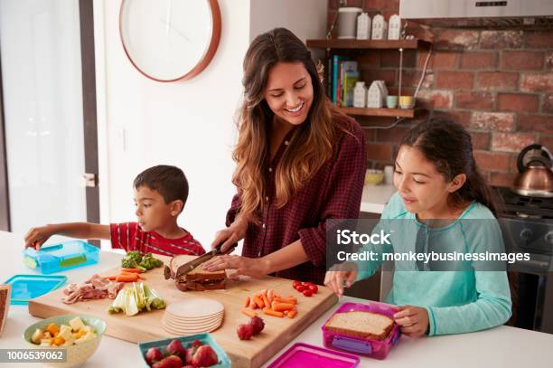 Niños Ayudando A Madre A Hacer Escuela Almuerzos En Cocina En Casa Foto de stock y más banco de imágenes de Niño