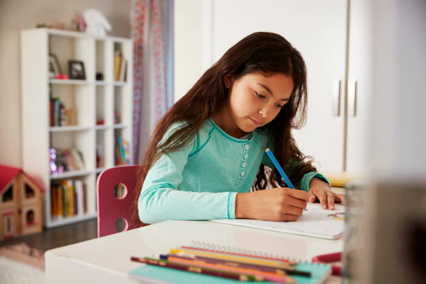 istock Young Girl Sitting At Desk In Bedroom Doing Homework 1006541740