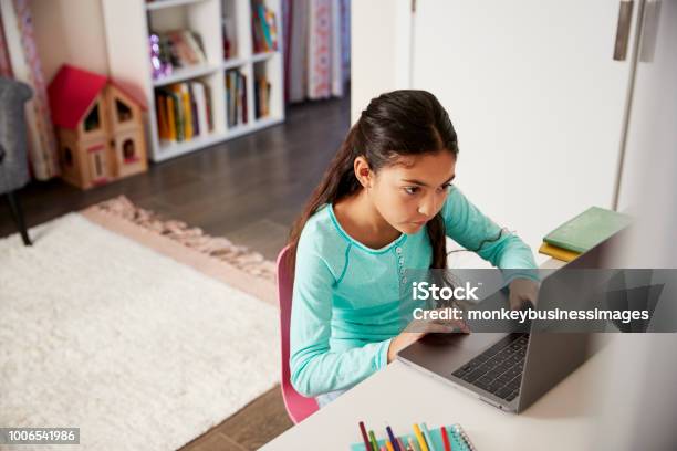 Young Girl Sitting At Desk In Bedroom Using Laptop To Do Homework Stock Photo - Download Image Now