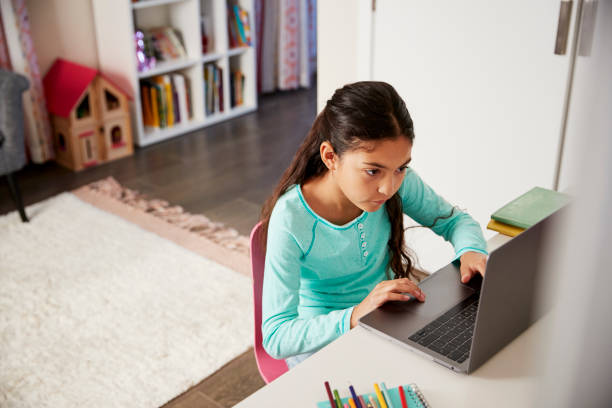 young girl sitting at desk in bedroom using laptop to do homework - homework imagens e fotografias de stock