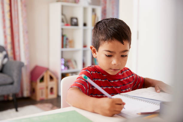 istock Young Boy Sitting At Desk In Bedroom Doing Homework 1006542804
