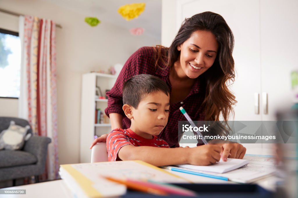 Mother Helping Son With Homework Sitting At Desk In Bedroom Child Stock Photo