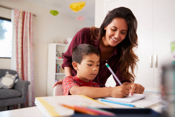 Mother Helping Son With Homework Sitting At Desk In Bedroom Mother Helping Son With Homework Sitting At Desk In Bedroom homework stock pictures, royalty-free photos & images