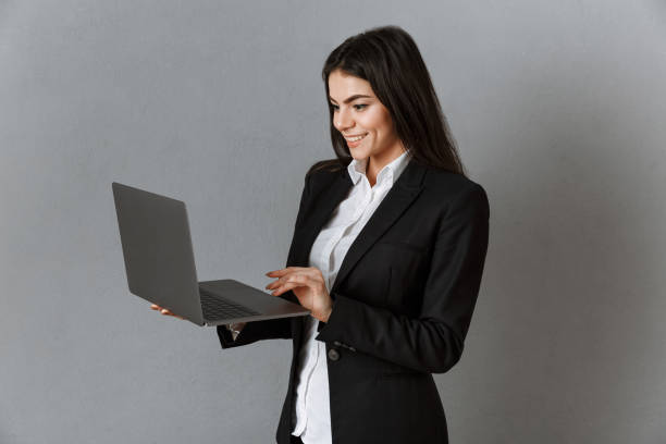 istock smiling businesswoman using laptop against grey wall background 1006546618