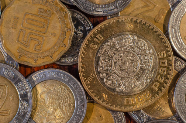 pièce de monnaie mexicaine au milieu d’autres pièces de monnaie sur une table de bois - number 10 gold business paper currency photos et images de collection