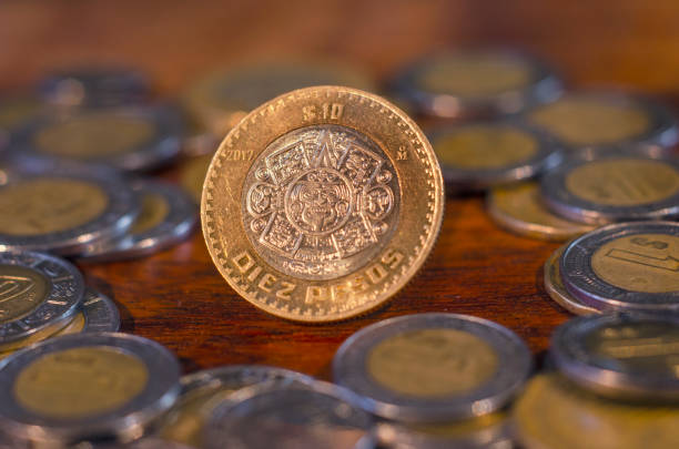 pièce de monnaie mexicaine au milieu d’autres pièces de monnaie sur une table de bois - number 10 gold business paper currency photos et images de collection