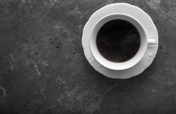 istock White cup of coffee on dark grey beton background decorated with coffee beans. Copy space 1006559048