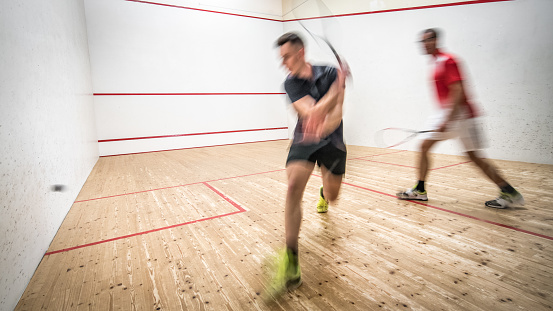 Male squash coach playing game of squash with his young male student.