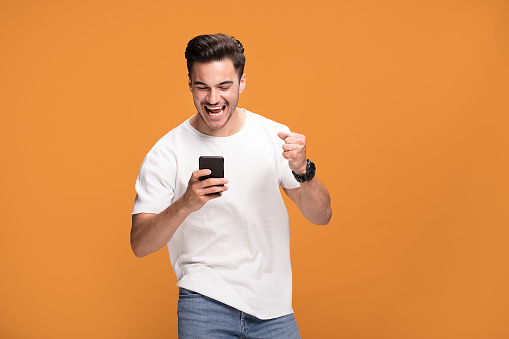 Handsome smiling excited man holding mobile phone posing on yellow studio background.