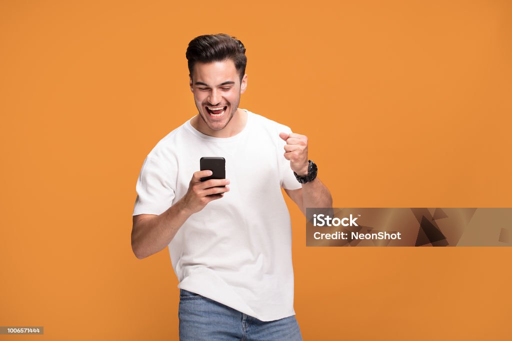 Smiling handsome man with mobile phone on yellow background. Handsome smiling excited man holding mobile phone posing on yellow studio background. Men Stock Photo