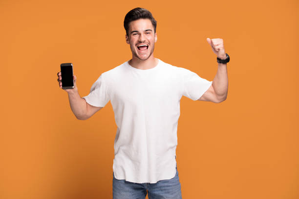 istock Smiling handsome man with mobile phone on yellow background. 1006571480