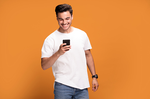Handsome smiling excited man holding mobile phone posing on yellow studio background.