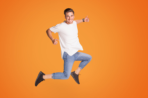 Full length photo of a smiling young man showing okay symbol and jumping isolated over yellow studio background. Happy handsome guy.