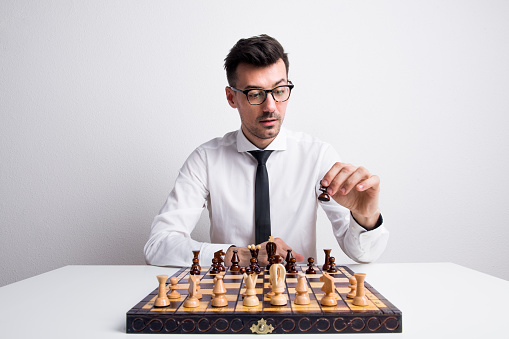 Portrait of a young man with white shirt and necktie in a studio, playing chess.