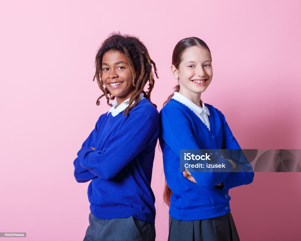Happy students standing together Happy young school children standing together with their arms crossed. Teenage boy and girl in school uniform looking at camera and smiling on pink background. School Uniform Stock Photo
