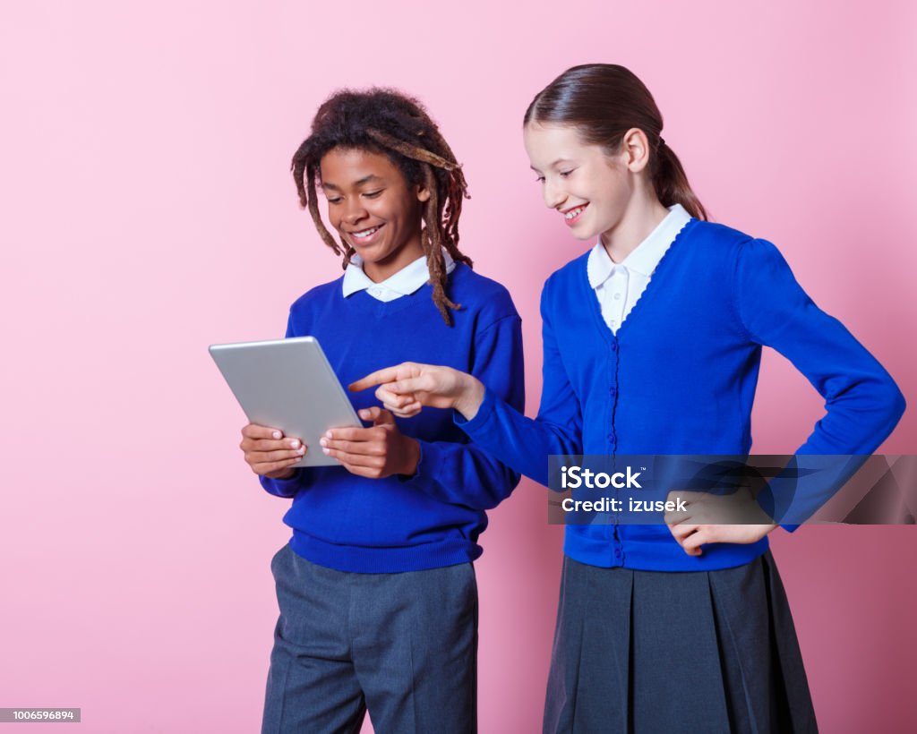 Two students using digital tablet Two students using digital tablet on pink background. Teenage boy and girl in school uniform looking at tablet pc. Teenager Stock Photo
