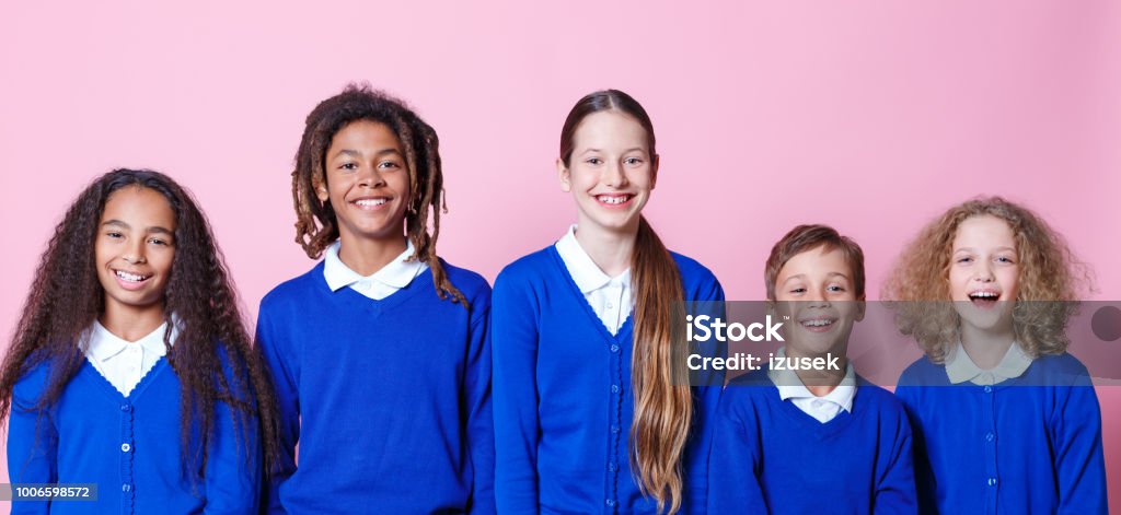 Group of smiling students Portrait of group of young students smiling against pink background. Children in school uniform standing together. Colored Background Stock Photo