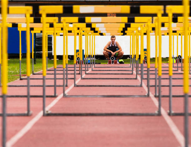 Front View of Young Athlete Through the Hurdles Poartrait of young male athlete ready for the 110 m race hurdling track event stock pictures, royalty-free photos & images
