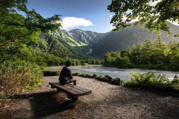 homem sentado no banco sozinho no parque nacional de kamikochi - bench mountain park sitting - fotografias e filmes do acervo