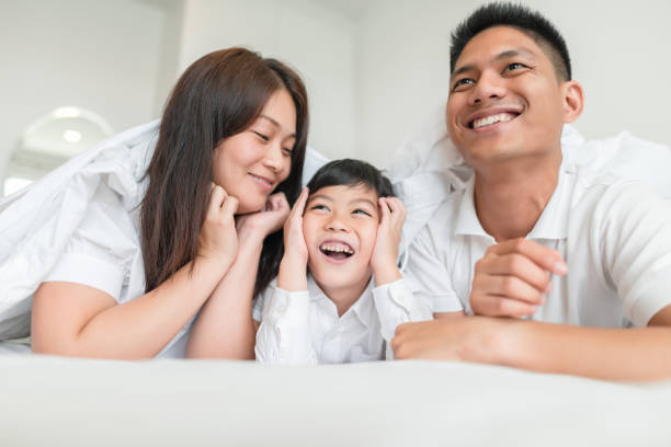 portrait happy family at home portrait happy family mom dad and son  smiling in bed room. look at each other. happy malay couple stock pictures, royalty-free photos & images