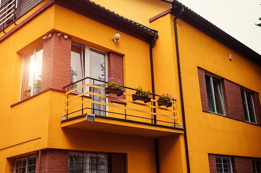 The new two-storey residential building with flowers on balcony. Cozy private house. Bright yellow house surrounded with garden
