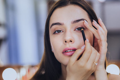 Black eyeliner. Unbelievably beautiful young dark-haired woman using black eyeliner while putting makeup on