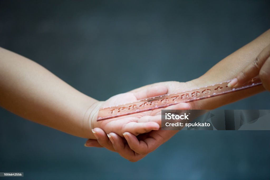 Student being physically punished by teacher with a ruler on on wooden blackboard or chalkboard background. Teacher Stock Photo