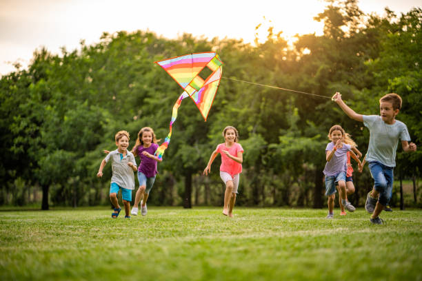 Happy kids running for a flying dragon Group of happy children running with a flying dragon in public park kite toy stock pictures, royalty-free photos & images