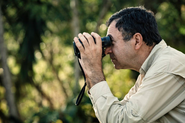 istock Hispanic mature man looking through binoculars on the forest 1006653402