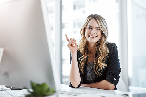 Portrait of a young businesswoman gesturing with her hand at her desk in a modern office