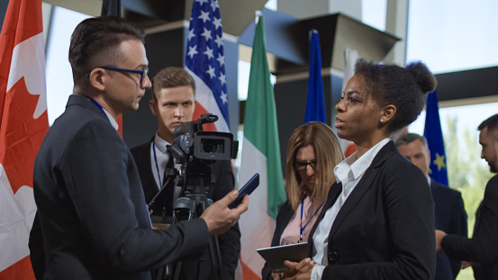 Formal African-American woman talking to journalist for camera and giving interview on international summit