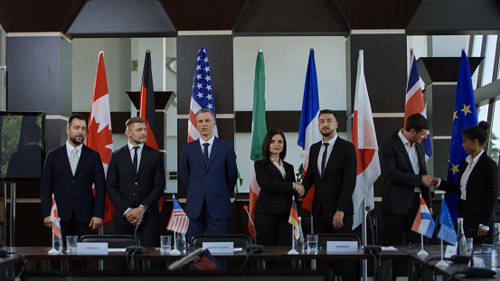 Members of Group of Seven taking photo against countries flags on international meeting in boardroom