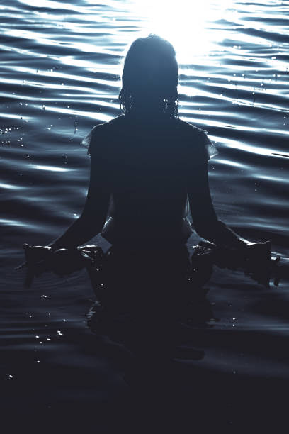 Ripples shadows and light Dark and gloomy scene of a young woman standing in shallow waters woman cold water swimming stock pictures, royalty-free photos & images