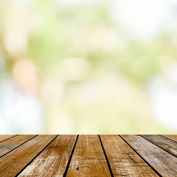 istock blur soft green nature background with glow sunny light and aged plain wood table top perspective view for promote or present product concept. 1006695934